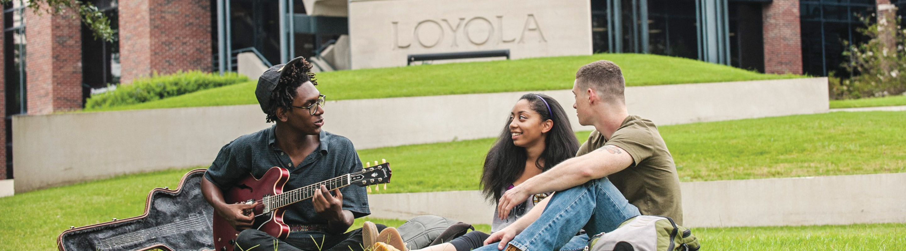 Three students on Monroe lawn with guitar