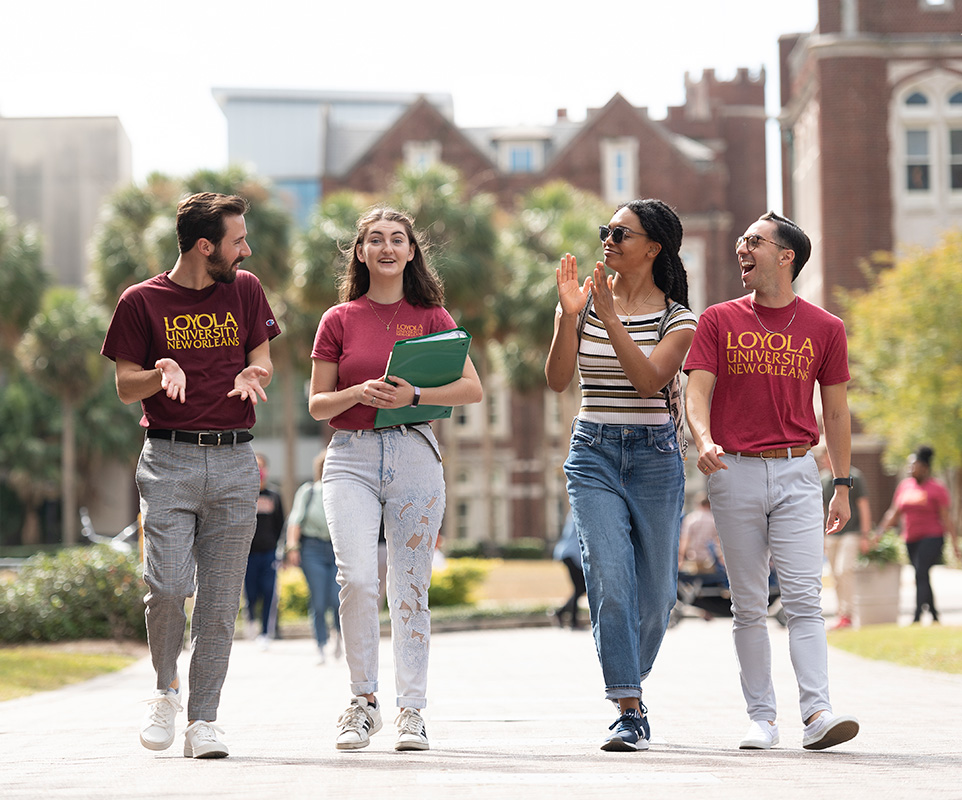 Four students have a lively conversation as they walk across campus.