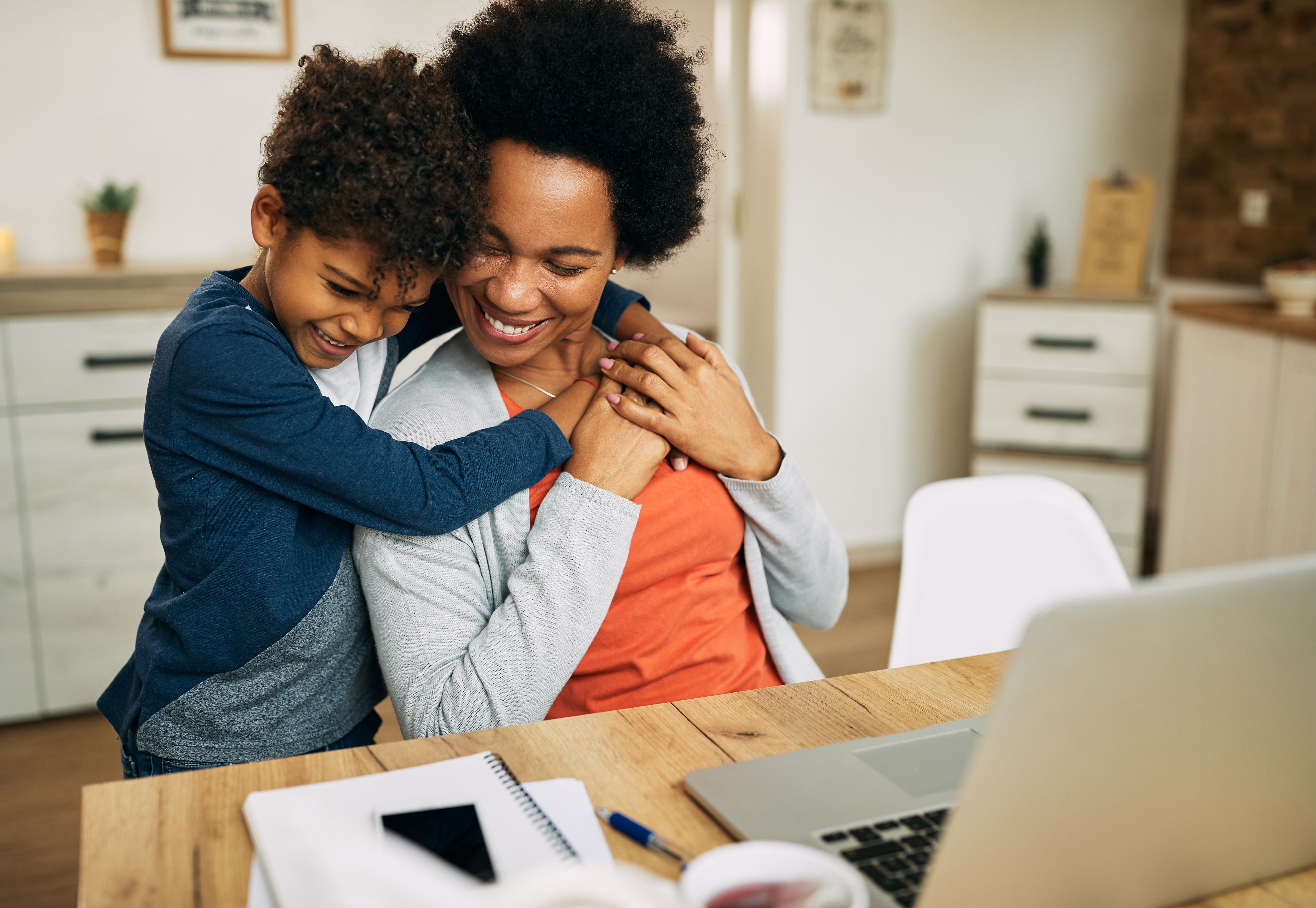 A child hugging their mother working on a laptop